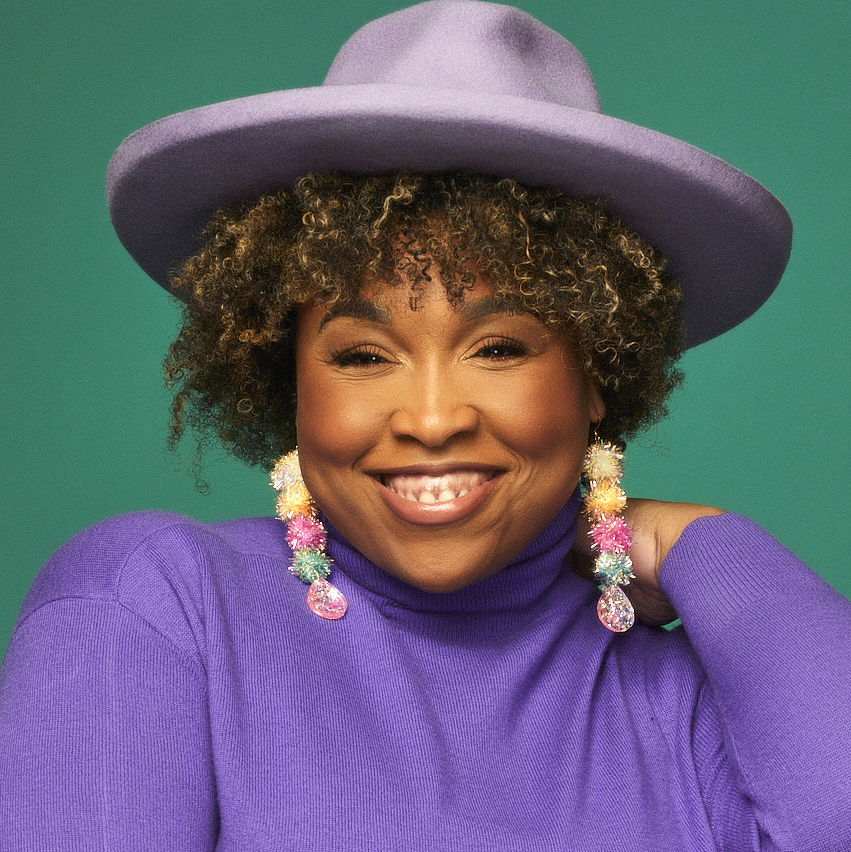 A headshot of a woman smiling in a purple shirt and hat